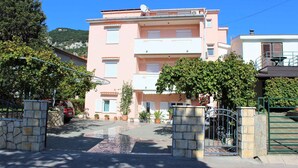 Un edificio a più piani con facciata rosa, ingresso carrabile con cancello e viale che conduce a un'auto parcheggiata.