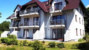 Ein zweigeschossiges Wohngebäude mit rotem Ziegeldach, mehreren Balkonen mit Metallgeländern und einer weißen Fassade.