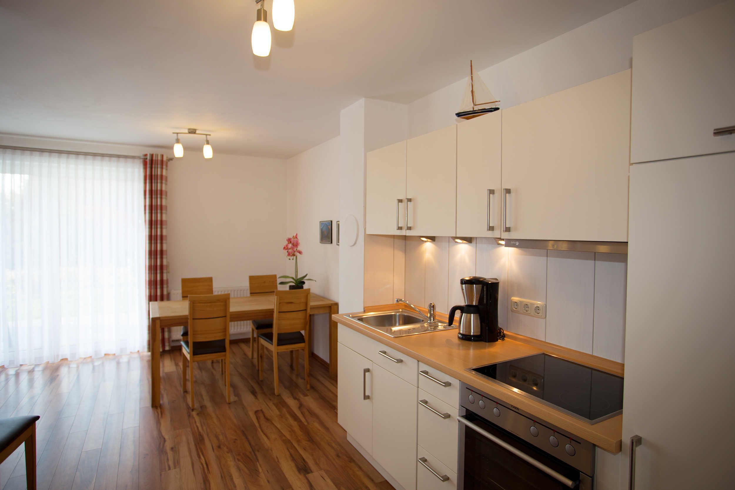 A modern kitchen with wooden flooring, white cabinets, a built-in oven, and a coffee maker.