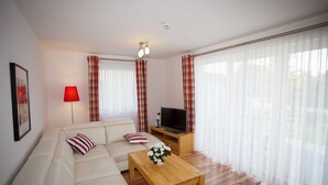 Ein Wohnzimmer mit einer Couch, einem Couchtisch, einem Fernseher auf einem Holzboden und einer Lampe.