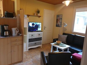 A cozy living room with a television, a coffee maker, and a small table with a bowl.