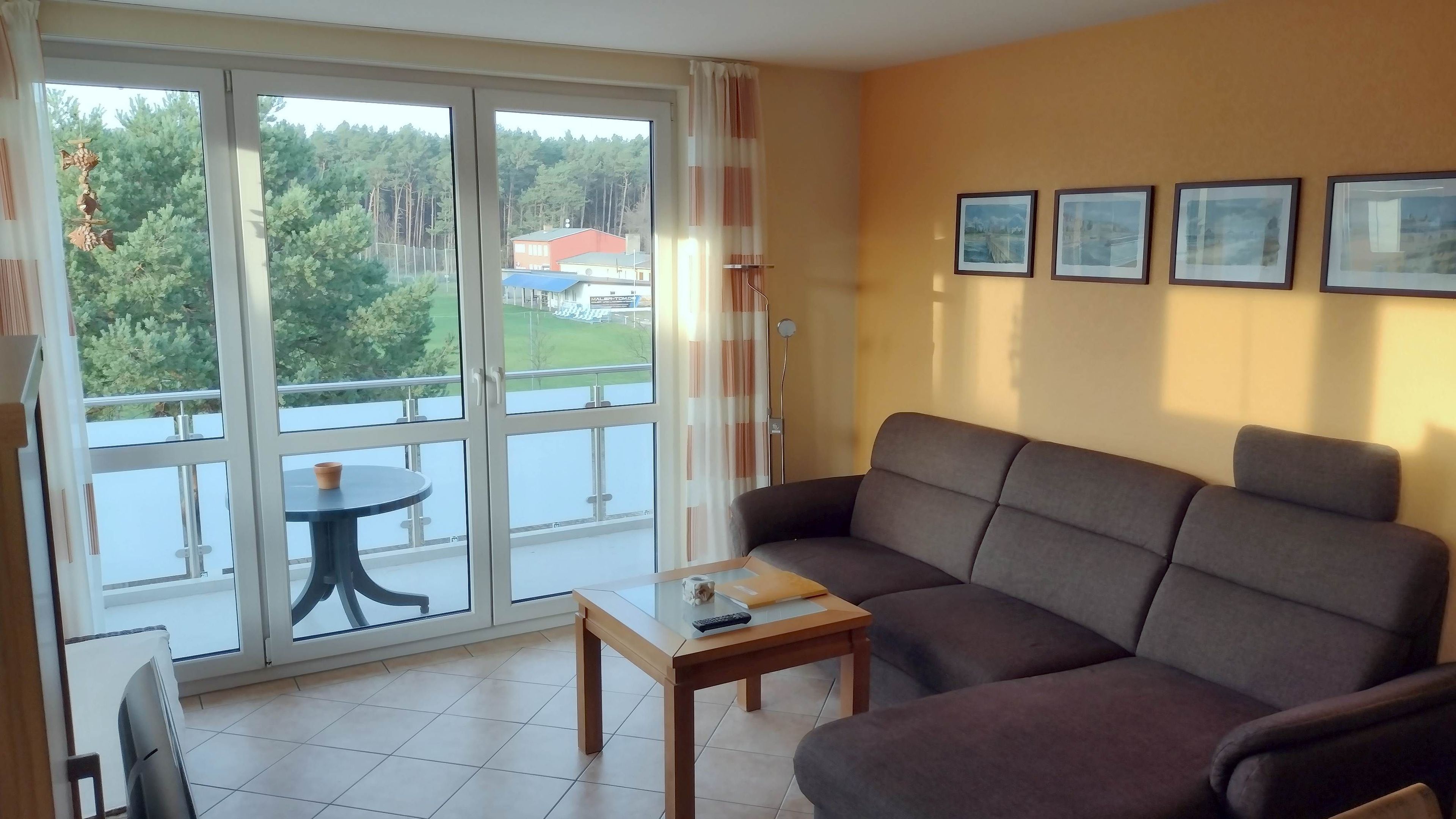 Ein Wohnzimmer mit einer Couch, einem kleinen Tisch und Blick auf einen Balkon mit Tisch und Stühlen.