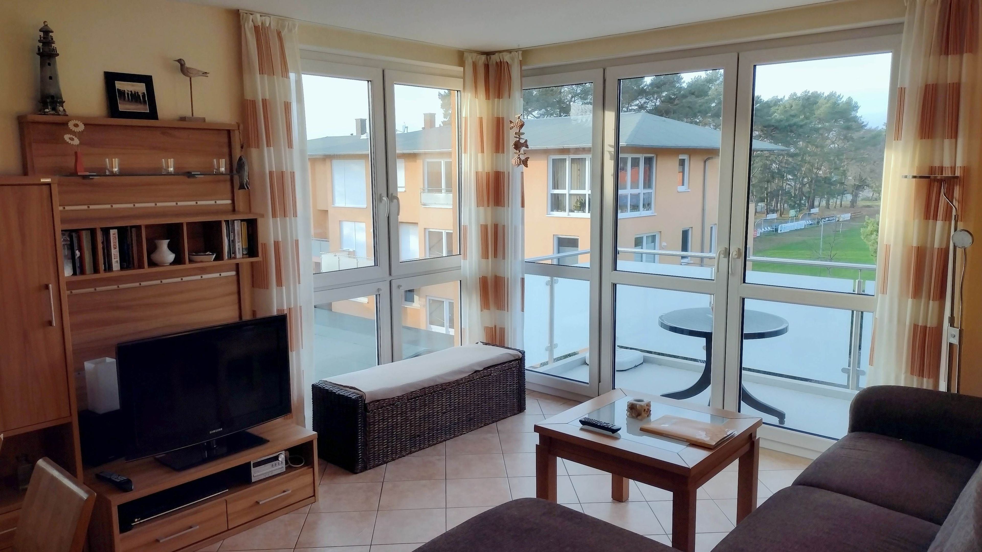 A living room with a TV, sofa, and a balcony with a table.