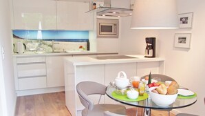 Cocina moderna con zona de desayuno que incluye una mesa de vidrio, sillas, un tazón de fruta y huevos.
