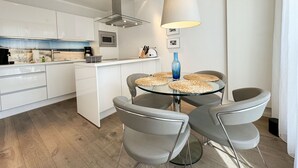 Una cocina moderna con armarios blancos, una isla central y una mesa redonda de comedor con cuatro sillas.