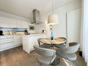 Cozinha moderna com armários brancos, uma ilha central e uma mesa de jantar redonda com quatro cadeiras.