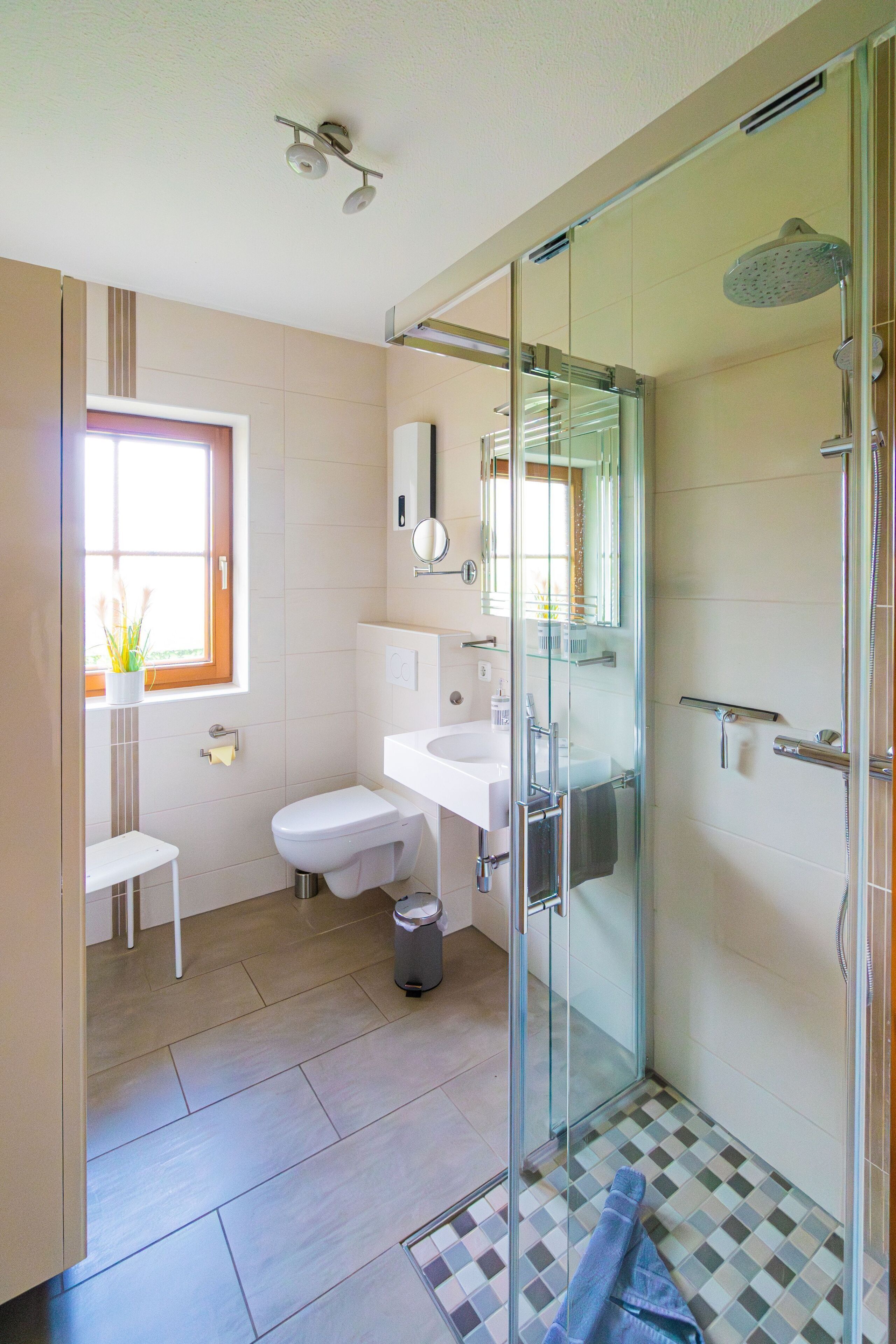 A modern bathroom with a glass-enclosed shower, a toilet, a sink, and a small window with a plant.