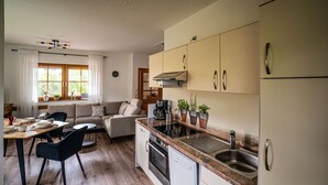 Una cocina moderna con horno integrado, lavavajillas y lavabo. Cuenta con un comedor con mesa y sillas, y un sofá.