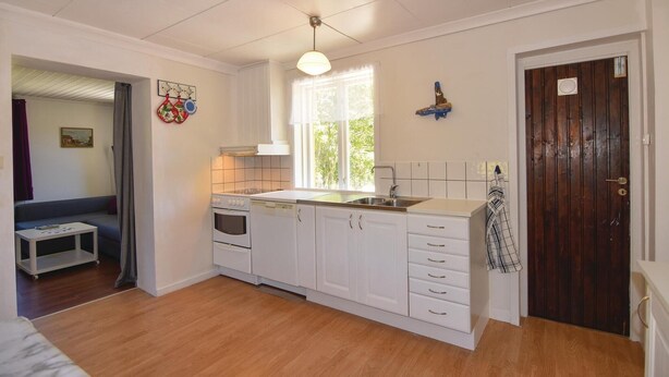 A compact kitchen with white cabinets, a stove, and a window. There is a wooden door and a small table with a chair. - Awesome home in Hunnebostrand (Hunnebostrand)
