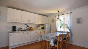 A compact kitchen with white cabinets, a dining table with chairs, a refrigerator, and a coffee maker. - Awesome home in Hunnebostrand (Hunnebostrand)