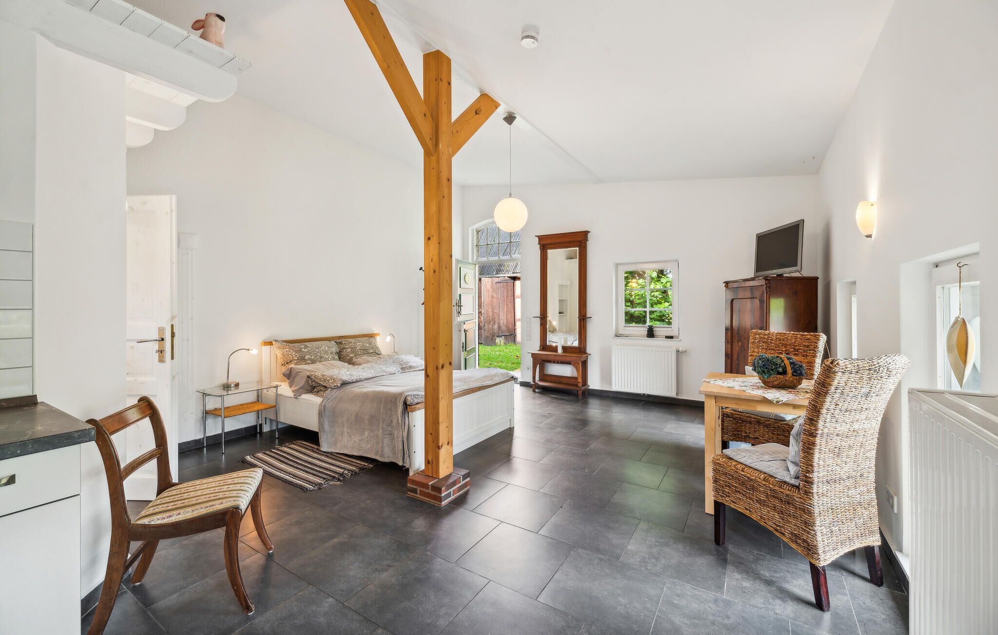 Una habitación amplia con una cama, una mesa de comedor y una silla de mimbre.