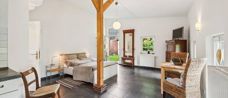 Una habitación amplia con una cama, una mesa de comedor y una silla de mimbre.
