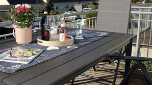 Een tafel met een tijdschrift, een vaas met bloemen, een fles wijn en glazen op een terras.