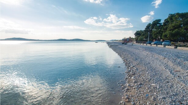 Una playa de guijarros con agua tranquila, una isla a lo lejos y un cielo despejado.