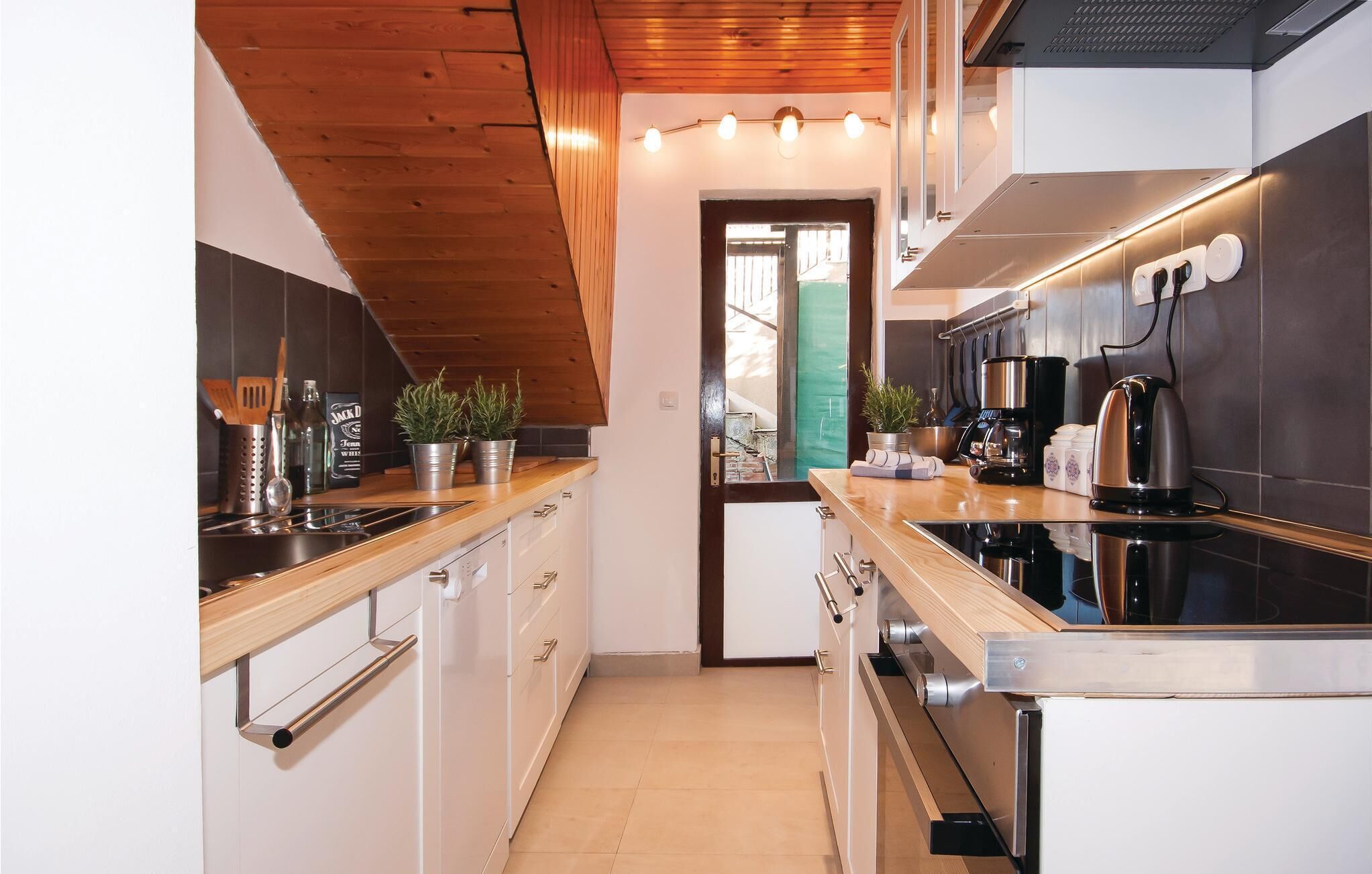 A modern kitchen with wooden ceiling, stainless steel appliances, and a view to the outside.