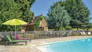 Ein Schwimmbecken mit einer Steindeck, einem Holzzaun und einem Steinhaus im Hintergrund.