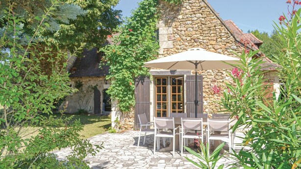 Ein Steinhaus mit einer gefliesten Terrasse, Sitzgelegenheiten im Freien und üppigem Grün.