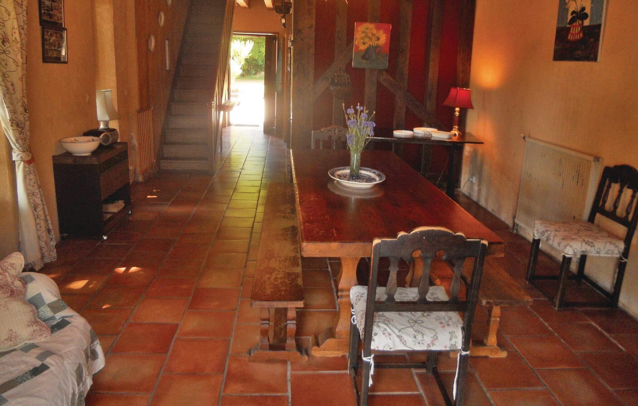 A dining area with a wooden table, chairs, and a vase of flowers. A staircase leads to another room.