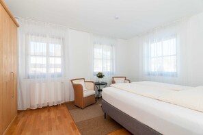 A bedroom with a bed, two chairs, a small table, and a window with curtains.