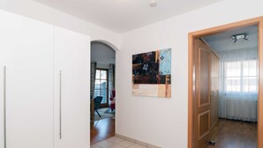 Een gang met een witte deur, een houten deur en een schilderij aan de muur.