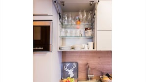 Een keuken met een ingebouwde oven, een spoelbak en een glazen plank boven het aanrecht met divers servies.