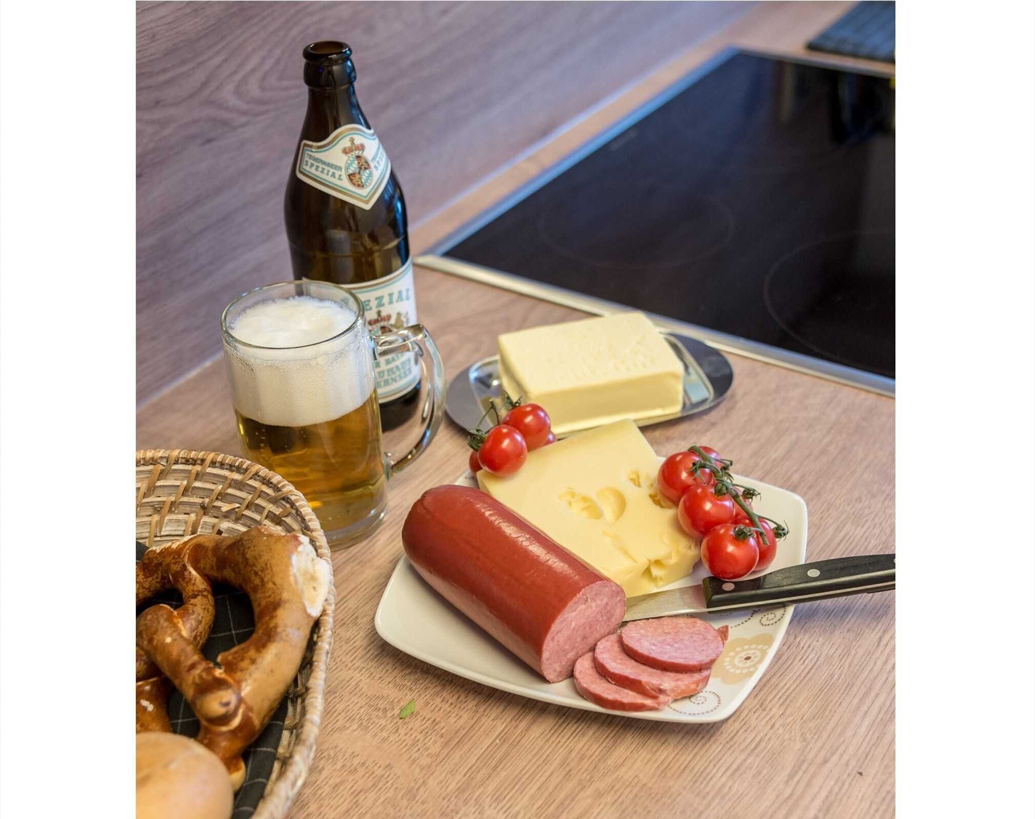 Une table avec une bouteille de bière, un verre de bière, une assiette de fromage, des tomates et des tranches de saucisson.