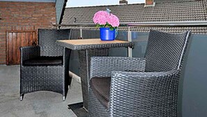 A rooftop patio with wicker furniture, a table, and a potted plant.