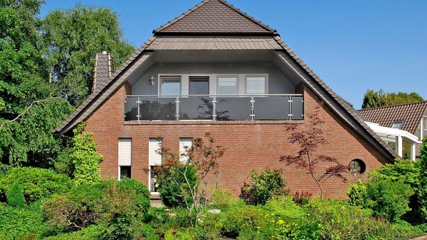 A two-story house with a brick exterior, a balcony on the upper floor, and a chimney.