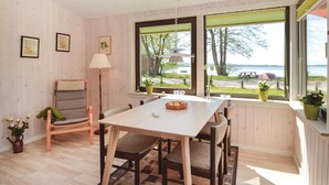Ein gemütliches Zimmer mit Holztisch und Stühlen, einer Stehlampe und Blick auf einen See durch große Fenster.