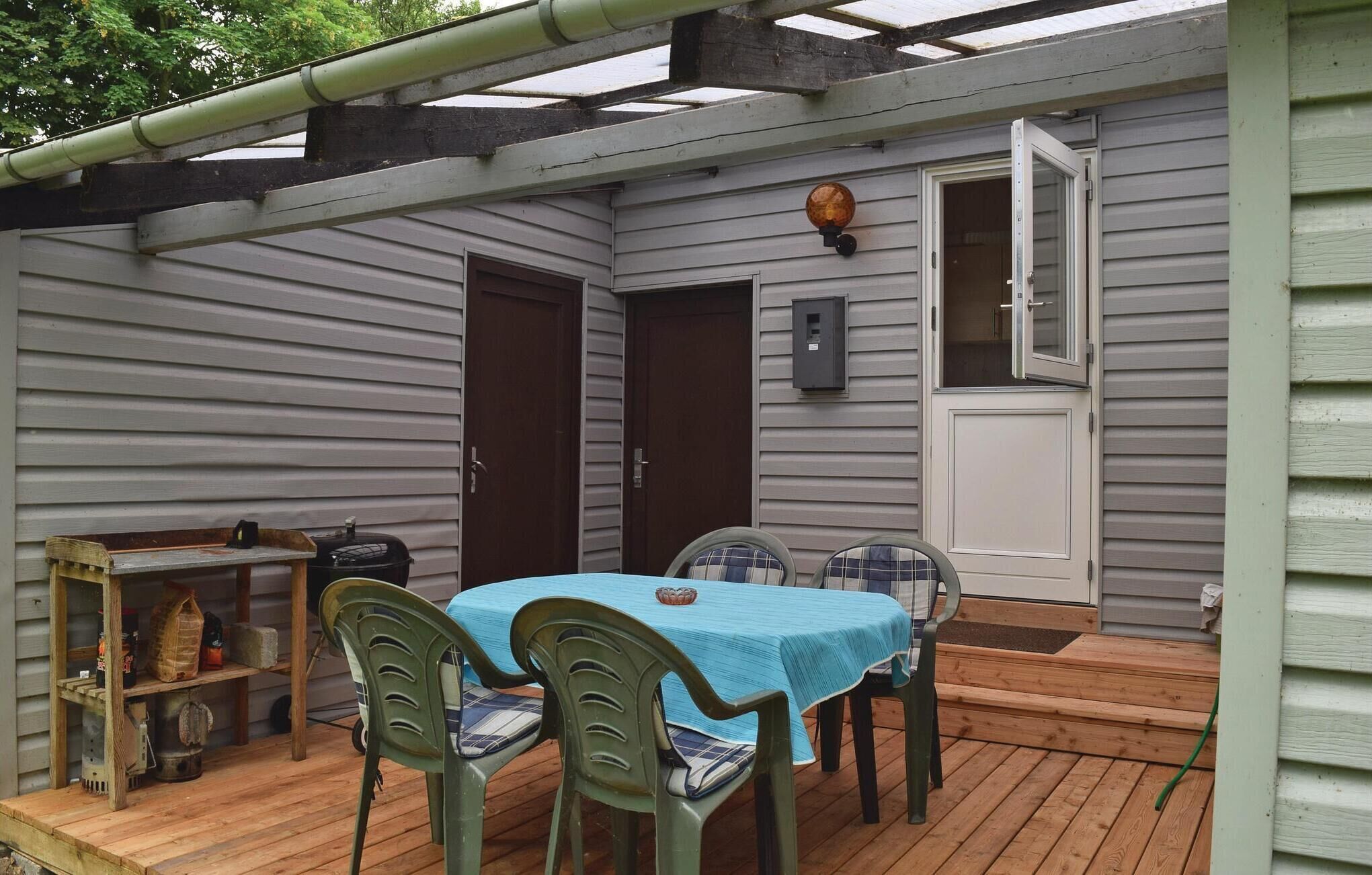 Eine überdachte Terrasse mit Tisch, Stühlen, einer Holzbank und einem Grill.