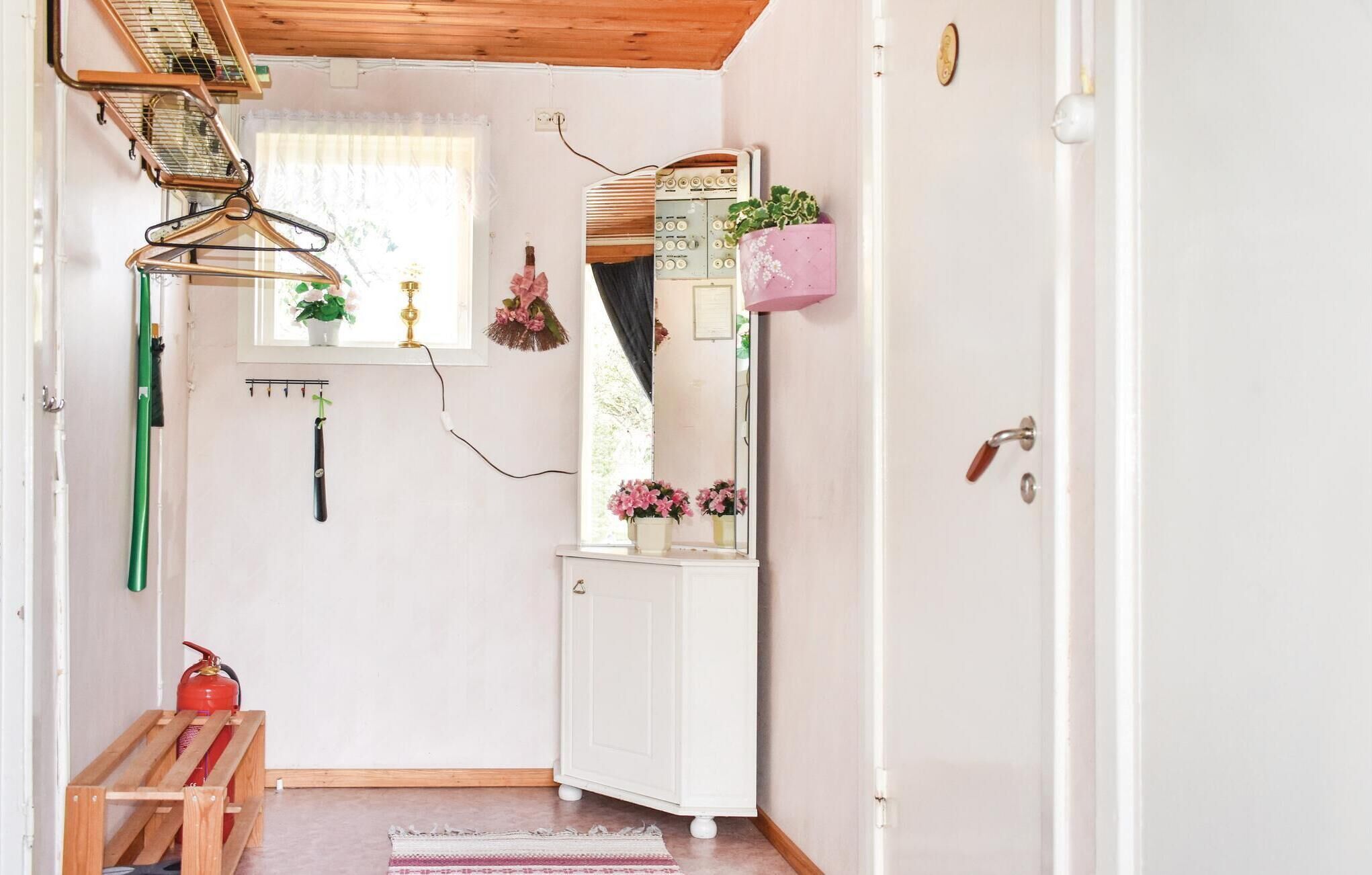 Un couloir avec une porte blanche, un miroir, une plante rose et un extincteur.