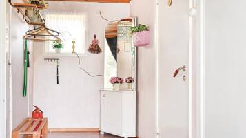 Un couloir avec une porte blanche, un miroir, une plante rose et un extincteur.