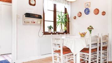 Un coin repas avec une table et des chaises blanches, une horloge au mur et divers objets décoratifs.