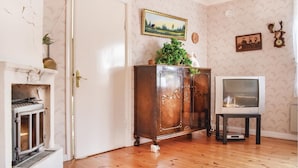 A room with a wooden floor, a white door, a fireplace, a cabinet with decorative carvings, a television, and wall-mounted pictures. - 2 bedroom lovely home in Järnforsen (Järnforsen)