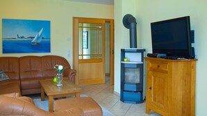 A living room with a brown leather sofa, a wooden coffee table, a painting of a sailboat, a fireplace, and a television on a wooden cabinet. - FH Lena to the beach only a few minutes walk ca.200 m quiet - FH Lena to the beach only (Glowe)