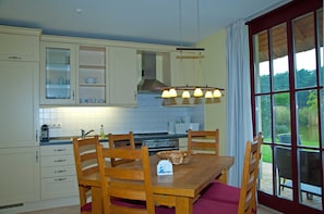 A kitchen with white cabinets, a dining table with chairs, and a view through a large window.