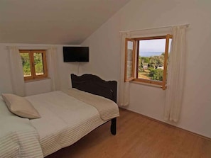 Een slaapkamer met een bed, een televisie aan de muur en een raam met uitzicht op groen.