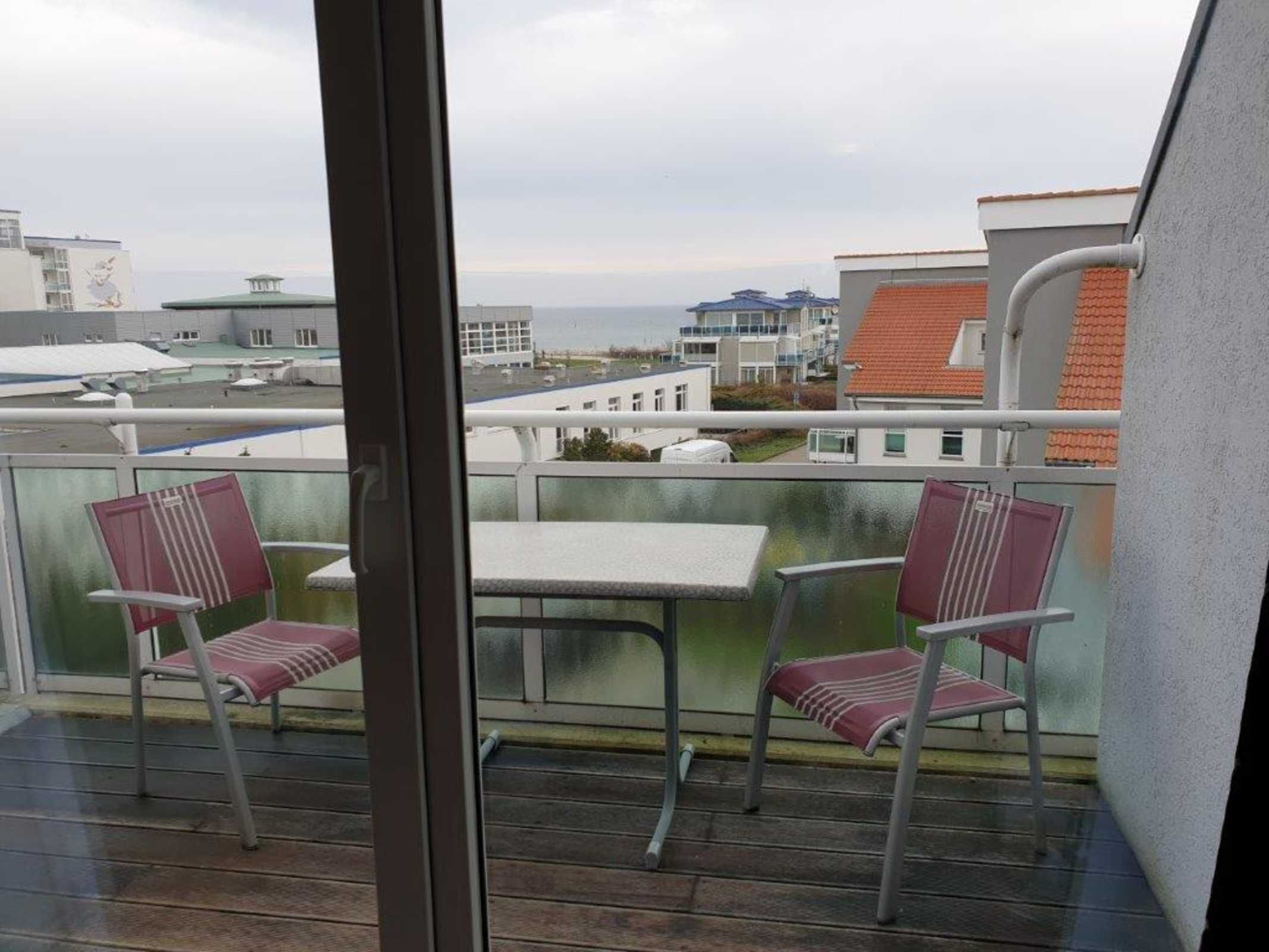 Un balcon avec deux chaises et une table, donnant sur un paysage urbain avec des immeubles et une vue sur la mer.