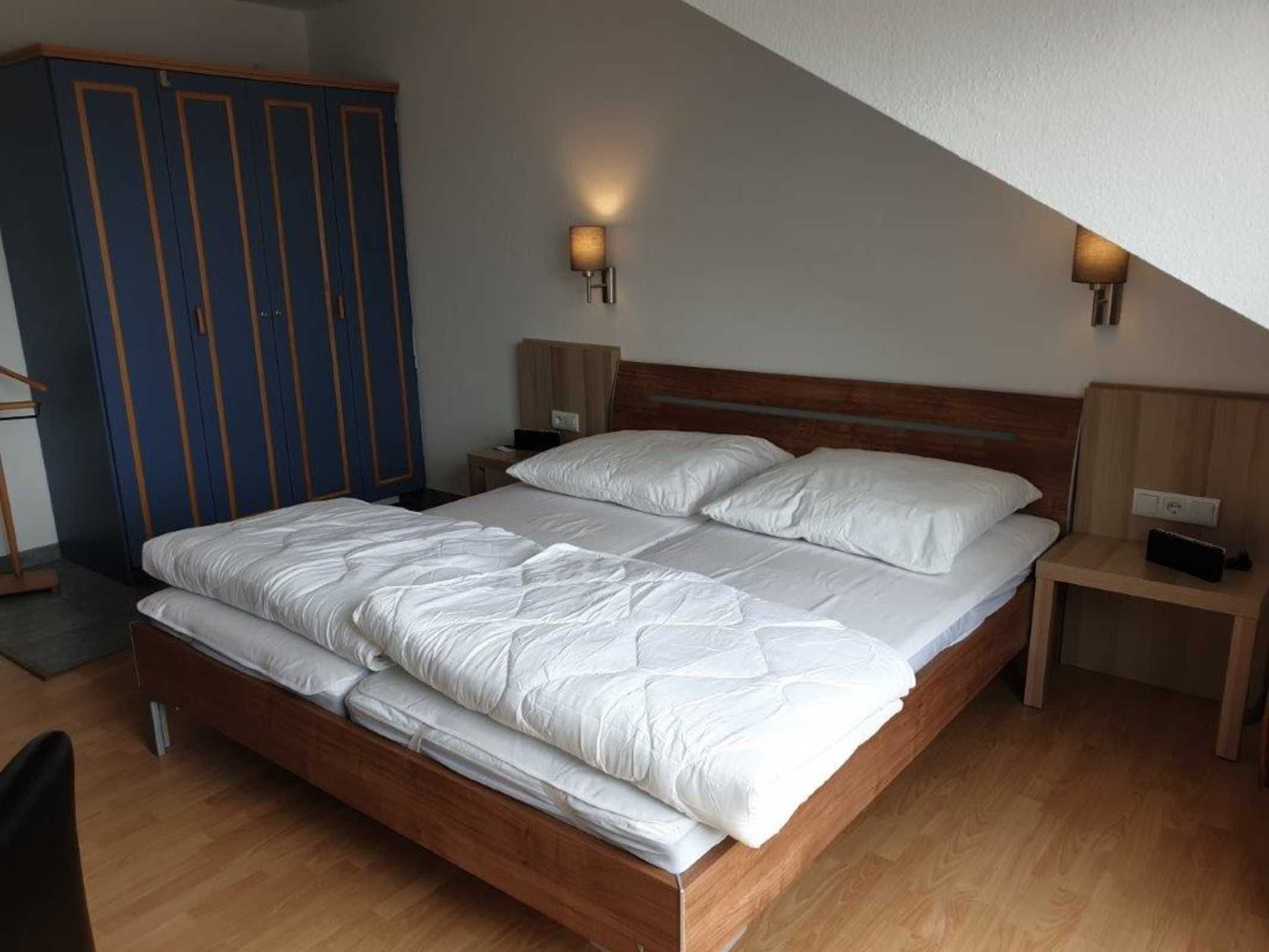 A bedroom with a wooden bed, two bedside tables, a wardrobe, and two wall-mounted lamps.