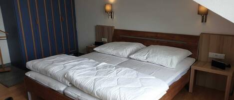 A bedroom with a wooden bed, two bedside tables, a wardrobe, and two wall-mounted lamps.