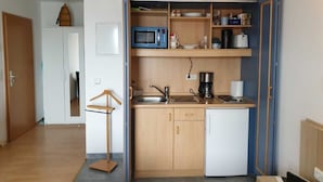 Cozinha compacta com micro-ondas, cafeteira e pequeno frigorífico.