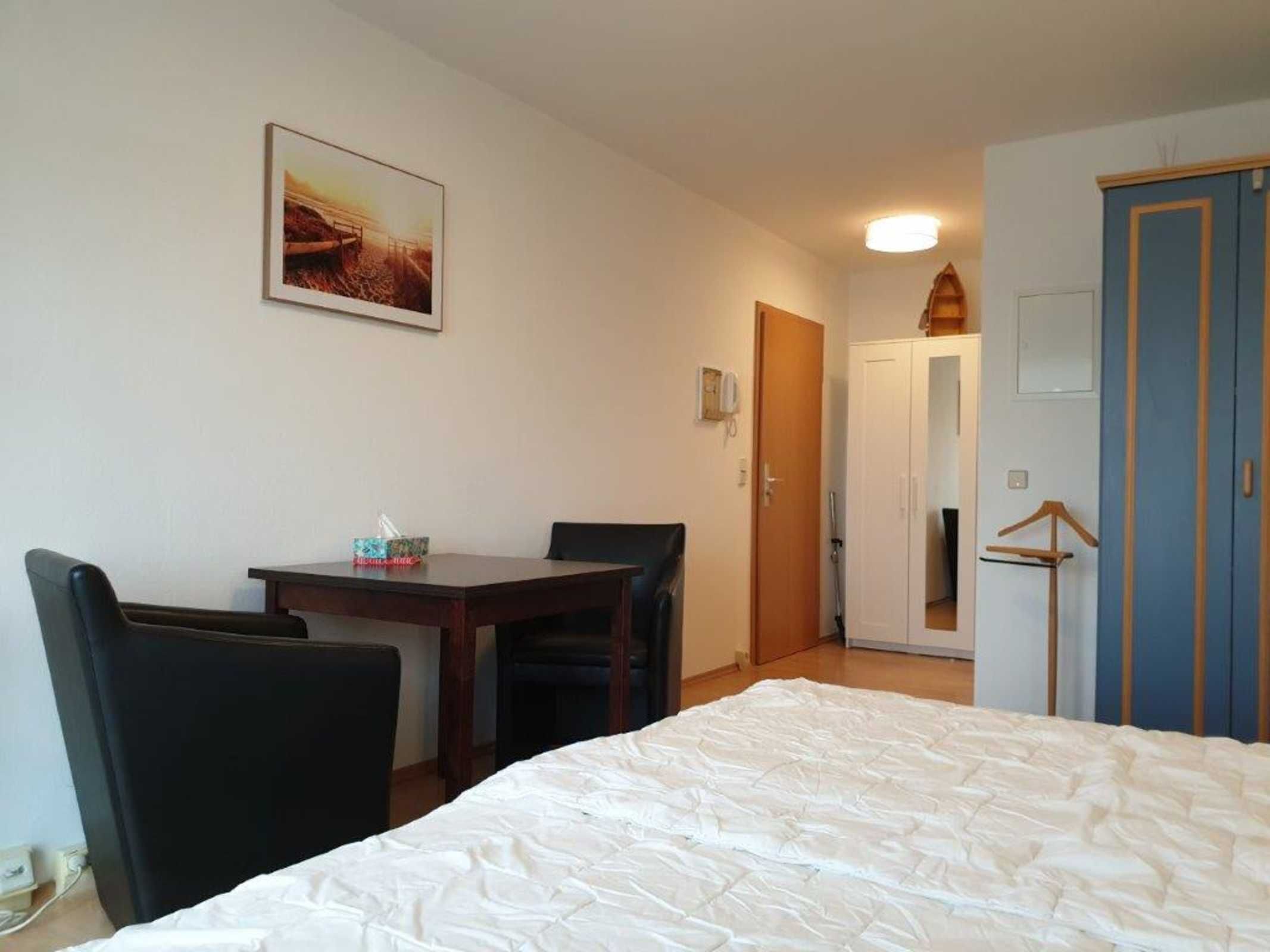 Habitación de hotel con cama, escritorio, dos sillas, perchero y puerta que da a otra habitación.