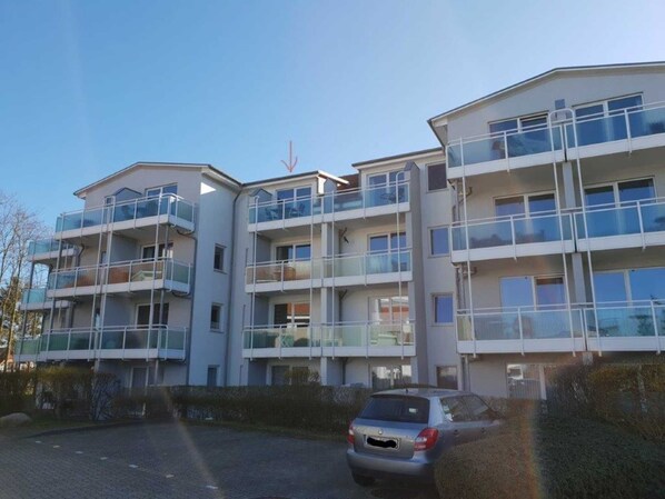 A multi-story residential building with balconies, a car parked in front, and a clear sky. - (272) 1-room apartment - apartment complex Yachthafenresidenz (Kühlungsborn)