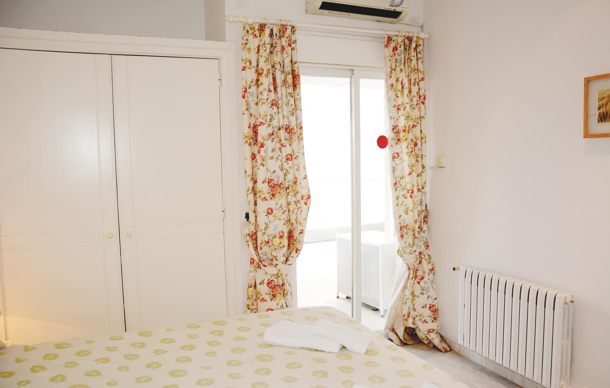 Une chambre à coucher avec un lit, des rideaux à motifs floraux, un radiateur et une porte blanche.
