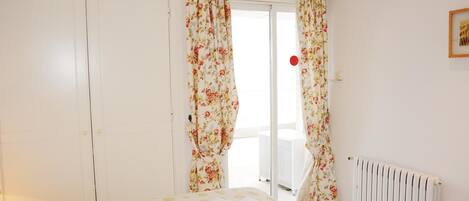 Une chambre à coucher avec un lit, des rideaux à motifs floraux, un radiateur et une porte blanche.