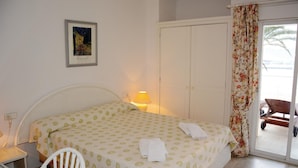 A bedroom with a bed, a nightstand, a chair, a door, and a window with curtains.
