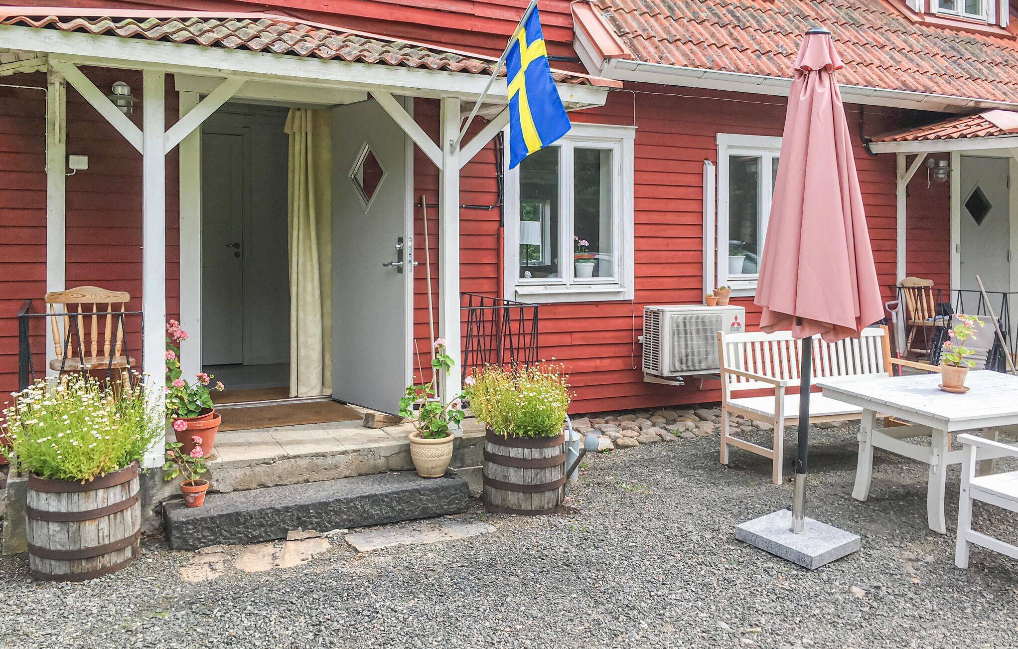 A red house with a porch, potted plants, a flag, and outdoor furniture.