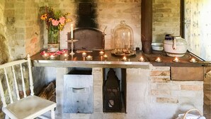 Un rustico camino in pietra con mensola bianca, candele accese, una cupola in vetro e una sedia bianca.