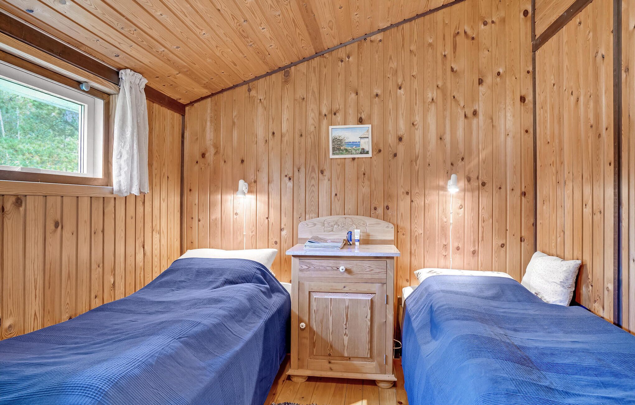 A cabin with two beds, wooden walls, a small desk, and a window with curtains.