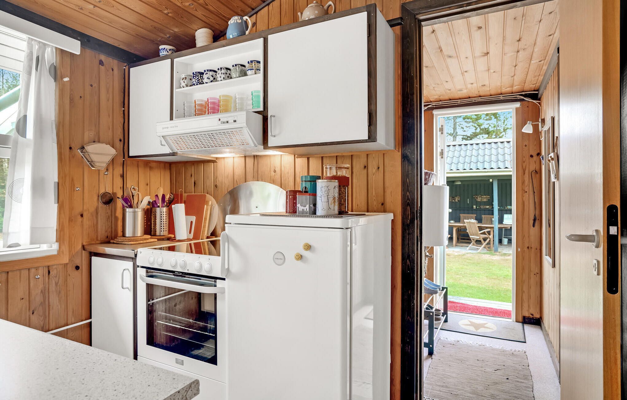 A compact kitchen with wooden walls, a built-in oven, and a refrigerator.